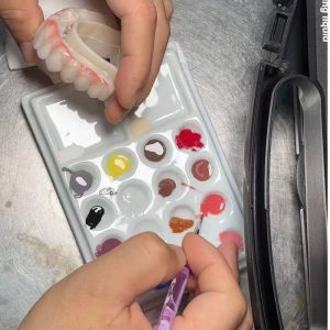 Dental technician applying Polyfix resin stains to a denture with color palette 